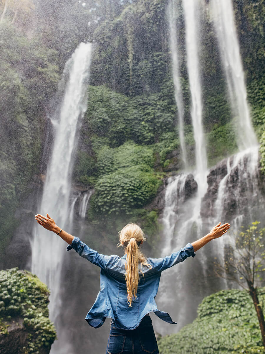 Person stretching out arms in front of a waterfall